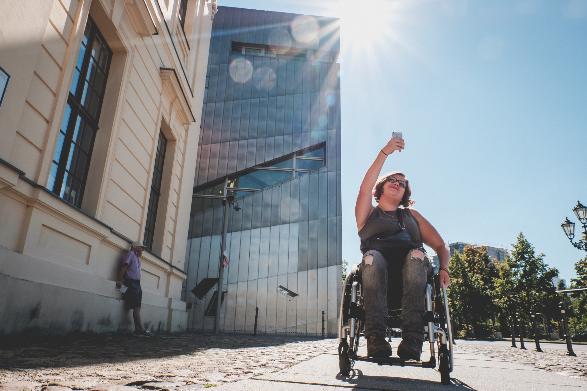 Eine Frau mit Rollstuhl reißt die Faust in die Luft, während sie an einem Gebäude vorbeifährt.