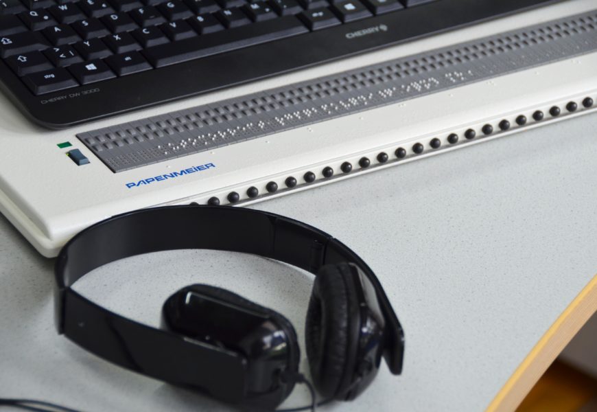 Eine digitale Braillezeile auf einem Schreibtisch, davor liegt ein Kopfhörer.