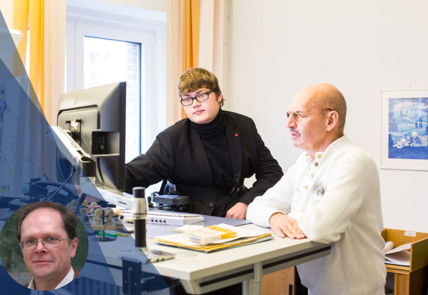 Ein Mitarbeiter mit Schwerbehinderung an seinem Büro-Arbeitsplatz, zusammen mit einem Kollegen.