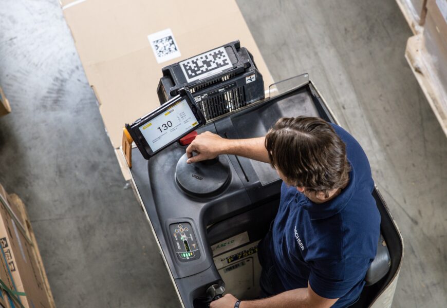 Mann steuert in Lagerhalle einen Gabelstapler mit digitalem Display