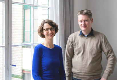 Sally Ollech (links) und René Kuhlemann (rechts) stehen in einem hellen Büro von Diversicon und lächeln in die Kamera.