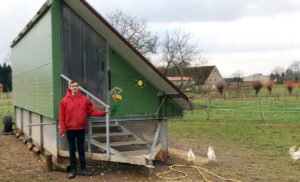 Manfred_Moning_Erlebnishof-Steckenpferd_Sonderpreis-Vorbild-Inklusion_64641_WEB Ein Mitarbeiter des Erlebnis-Bauernhofs steht auf einer Wiese vor einem mobilen Hühnerstall und schaut in die Kamera.