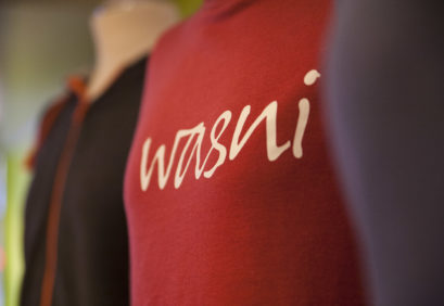 Bunte Pullis auf Schneiderpuppen, in der Bildmitte ein roter Pulli, auf dem "wasni" steht.