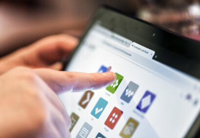 Ein Finger tippt auf ein grünes Symbol in der Lwerk-App auf einem Tablet-Bildschirm mit mehreren bunten App-Symbolen.